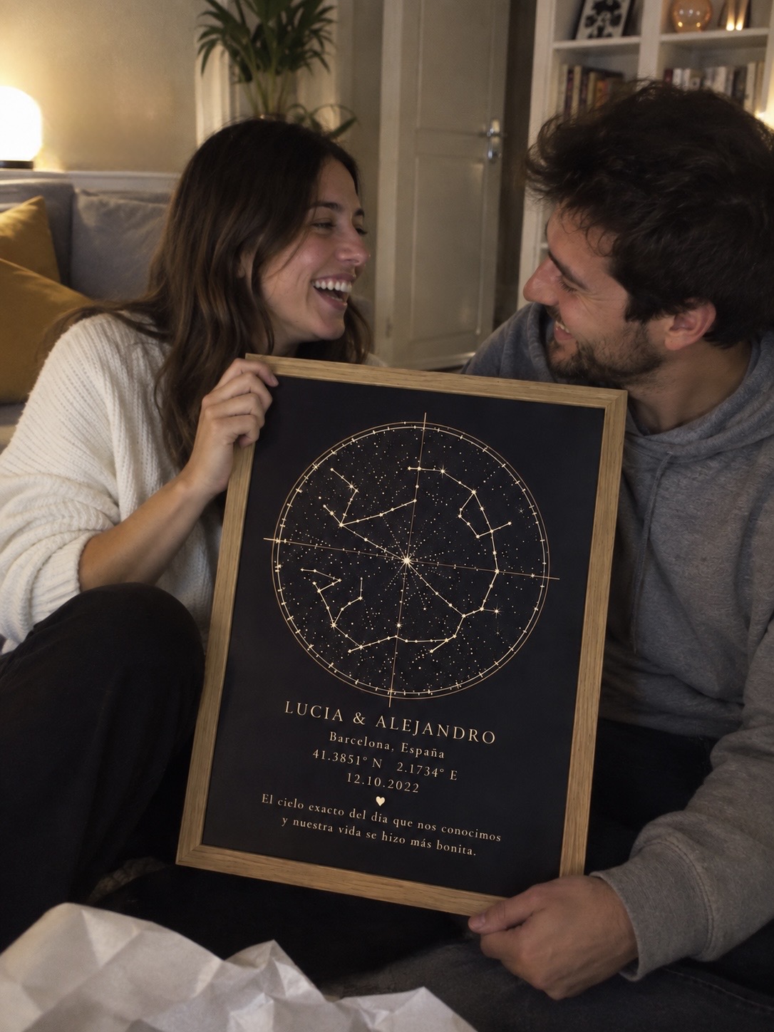 Pareja sonriendo mientras sostiene un mapa estelar con moldura de madera y detalles dorados